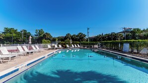 A swimming pool with clear blue water, surrounded by white lounge chairs and a fence.