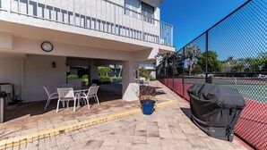 A patio area with outdoor seating, a covered grill, and a tennis court.