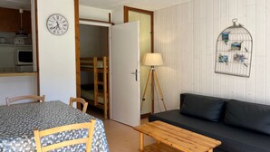 A compact room with a bunk bed, a dining table with chairs, a sofa, a lamp, and a wall clock.