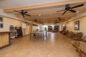 Eine geräumige Lobby mit einer Rezeption, mehreren Deckenventilatoren, einem großen Tisch und Korbmöbeln.