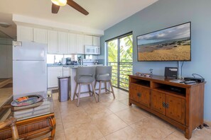 A modern kitchen with white cabinets, a microwave, and a large window. There is a dining area with two chairs and a table.