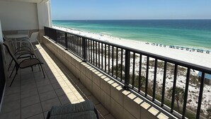 Ein Balkon mit Blick auf einen Strand, der ein Fliesenmuster, einen Tisch mit Stühlen und ein Geländer zeigt.