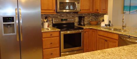 A modern kitchen with stainless steel appliances, granite countertops, and wooden cabinetry.