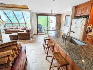Une cuisine moderne dotée d’un îlot central, de tabourets de bar et d’une grande fenêtre donnant sur une terrasse.