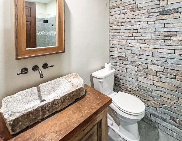 Une salle de bain avec un lavabo en pierre, un meuble-lavabo en bois, des toilettes et un mur en pierre.