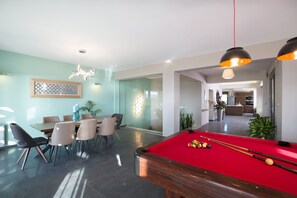 A modern living room with a pool table, dining area, and kitchen in the background.