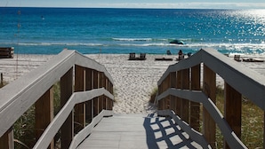 A wooden boardwalk leading to a sandy beach with a clear view of the ocean.