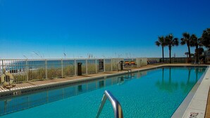 A clear blue pool with a metal railing, a wooden deck, and a fence.