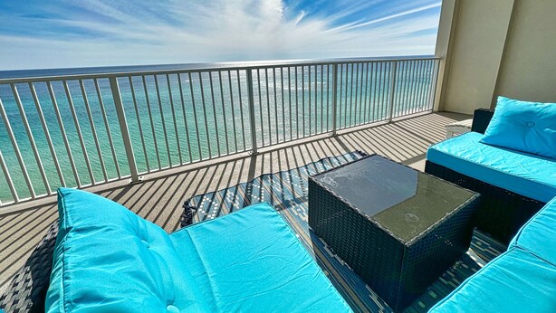 A balcony with a view of the ocean, a seating area with blue cushions, and a small table.