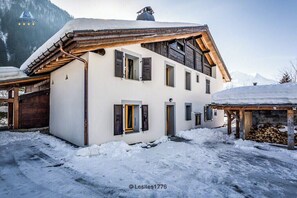 Un edificio blanco con vigas y contraventanas de madera, rodeado de nieve.