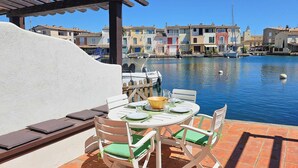 A terrace with a table set for dining, overlooking a marina with boats and colorful buildings.