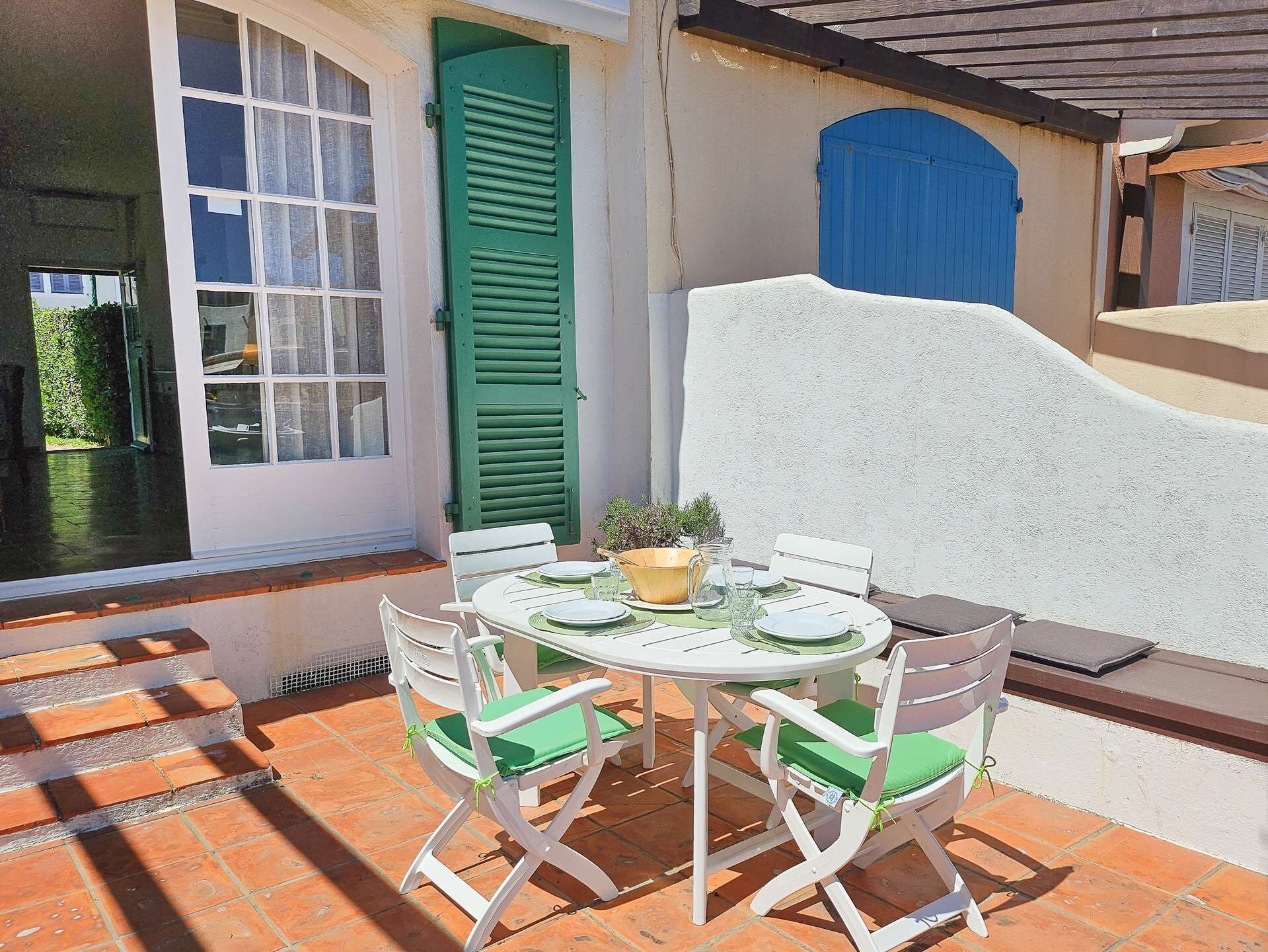 An outdoor patio with a round table and four chairs, a potted plant, and a blue door.