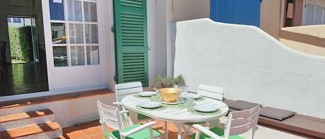 An outdoor patio with a round table and four chairs, a potted plant, and a blue door.