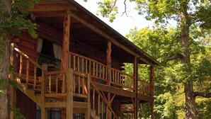 Une cabane en bois dotée d’un balcon et d’un escalier, entourée d’arbres.