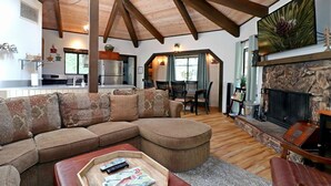 A cozy living room with a sectional sofa, a fireplace, and a dining area with a table and chairs. - Maple Bear: Walk to Snow Summit! Hot Tub! Game Room! Pool Table! Air Hockey! Internet! Family Friendly! (Big Bear Lake)