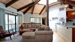 A cozy living area with a wooden ceiling, a sofa set, a dining table, and a kitchen area with a microwave. - Maple Bear: Walk to Snow Summit! Hot Tub! Game Room! Pool Table! Air Hockey! Internet! Family Friendly! (Big Bear Lake)