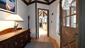 A hallway with wooden floors, a wooden dresser, a lamp with a deer silhouette, a red guitar, and a door with patterned curtains. - Maple Bear: Walk to Snow Summit! Hot Tub! Game Room! Pool Table! Air Hockey! Internet! Family Friendly! (Big Bear Lake)
