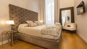 A bedroom with a tufted headboard, a bed with beige linens, a bedside table with a lamp, a chair, and a large mirror on the wall. - Amazing Piazza Venezia Suite Int 5 (Roma)