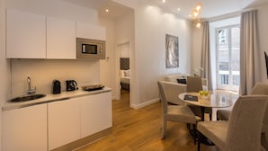 A modern kitchen with a built-in microwave, a coffee maker, and a sink. There is a dining area with a table and chairs, and a sofa in the background. - Amazing Piazza Venezia Suite Int 5 (Roma)