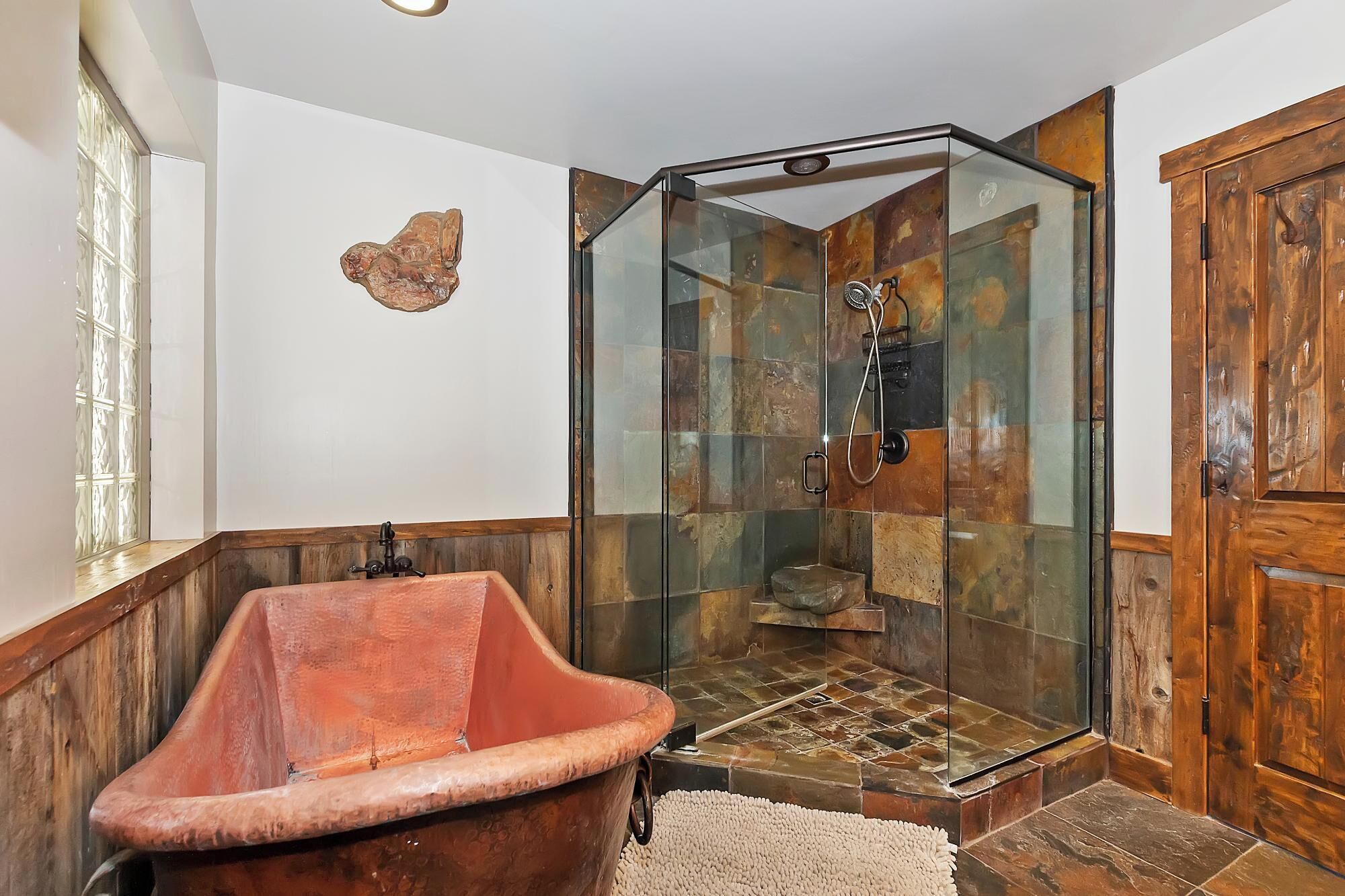 A bathroom with a glass shower enclosure, a wooden bathtub, and a stone-tiled shower floor.