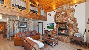 Un salon spacieux avec un haut plafond, une cheminée en pierre et une grande fenêtre donnant sur un paysage pittoresque.