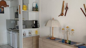 Una cocina con armarios blancos, una cafetera, una lámpara y una mesita con tazas y una planta.