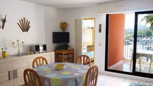 Un espacio habitable compacto con comedor, televisión y balcón con vistas a barcos.
