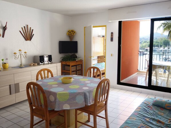 A compact living space with a dining area, a TV, and a balcony with a view of boats. - Studio cabin for 4 near the beach with parking in Argelès-sur-Mer (Argelès-sur-Mer)