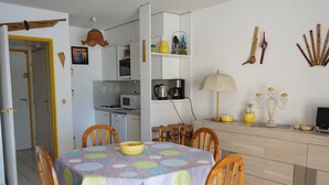 Un comedor con una mesa redonda cubierta por un mantel de lunares, rodeada de sillas de madera. Se ve una cocina al fondo con un microondas y una cafetera.