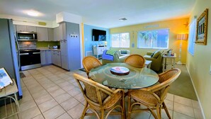 A compact kitchen with modern appliances, a dining area with wicker chairs, and a cozy living space with a sofa and a lamp. - 2nd House from the Beach with No Roads to Cross (Anna Maria)