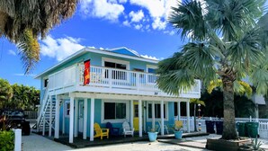 A two-story building with a balcony, numbered 207, featuring outdoor seating and potted plants. - 2nd House from the Beach with No Roads to Cross (Anna Maria)