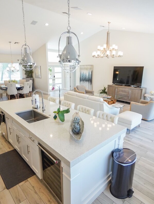 A modern kitchen with a large island, a dining area with a round table, and a living room with a sofa and TV.