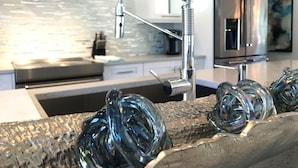 Une cuisine moderne dotée d’un robinet en acier inoxydable, d’une sculpture en verre et d’un réfrigérateur en acier inoxydable.
