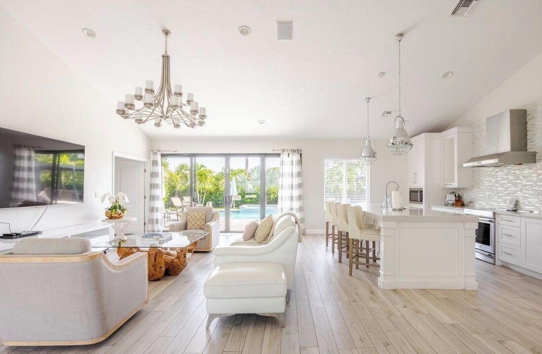 Un vaste espace de vie doté d’une grande fenêtre, d’un canapé blanc, d’une table à manger et d’une cuisine aux meubles blancs et au design moderne.