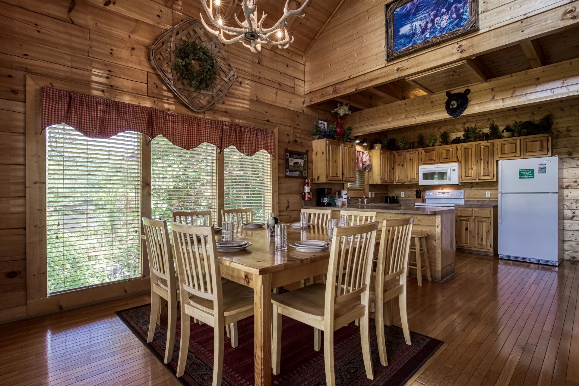 A wooden cabin interior with a dining area, kitchen, and large windows.