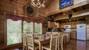 A wooden cabin interior with a dining area, kitchen, and large windows. - ERN849- Sweet Escape - Great Location! Close To Action! (Pigeon Forge)