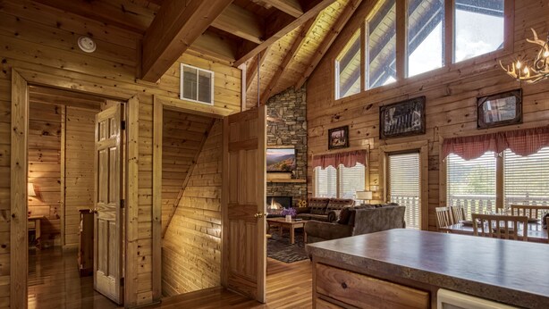 A wooden cabin interior with a kitchen, dining area, and a staircase leading to a loft. - ERN849- Sweet Escape - Great Location! Close To Action! (Pigeon Forge)