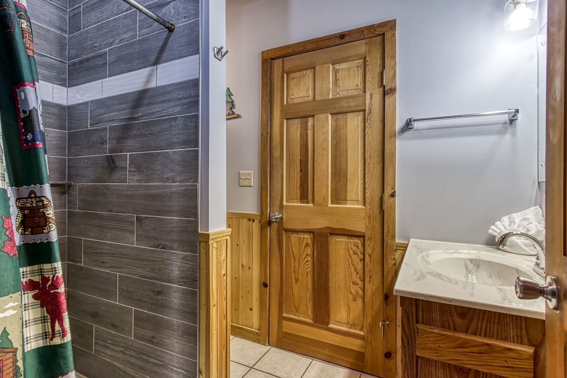 A bathroom with a wooden door, a white sink, and a shower area with dark tiles.