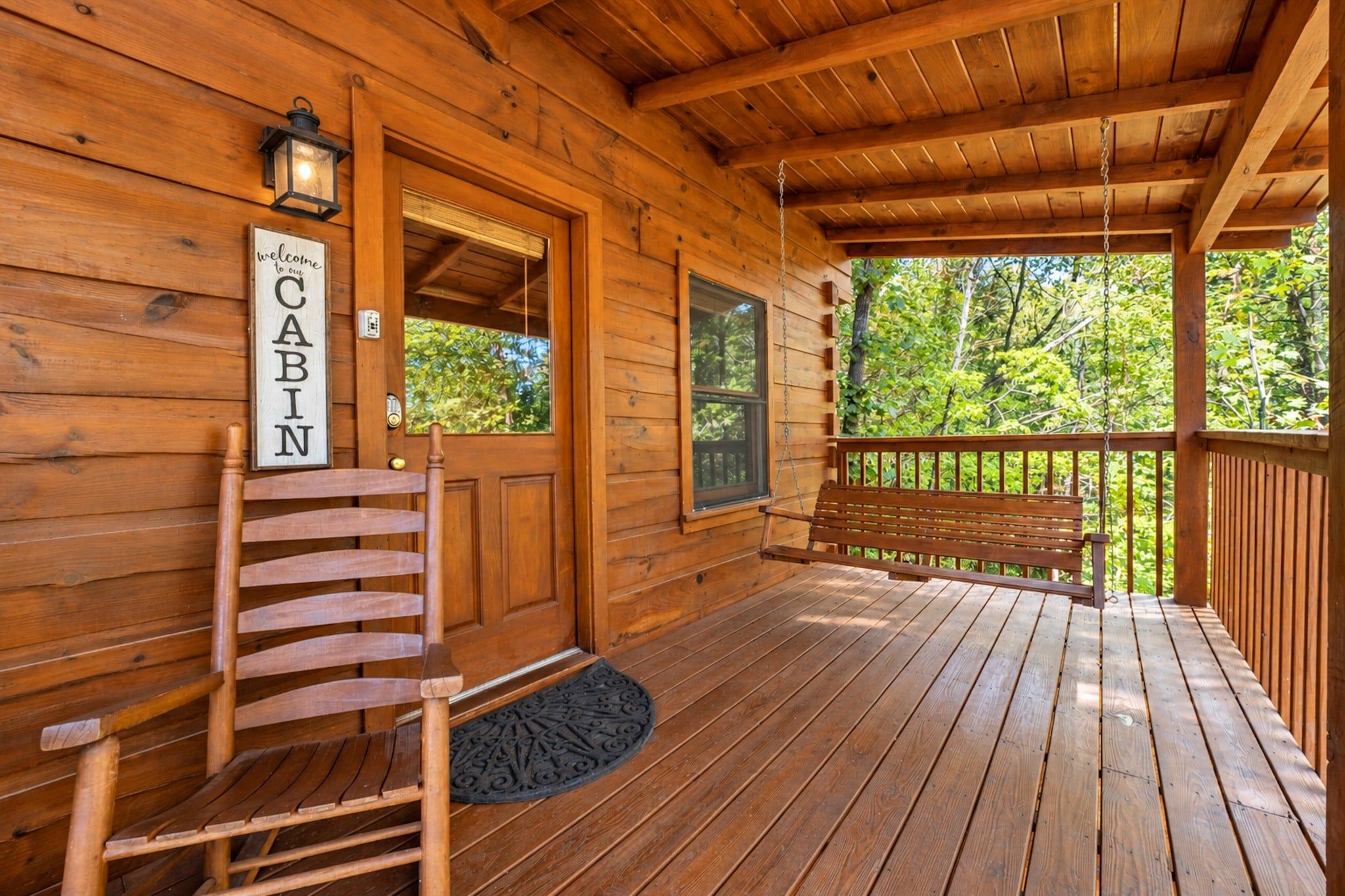 A wooden cabin with a porch, a bench, a door, and a welcome sign.
