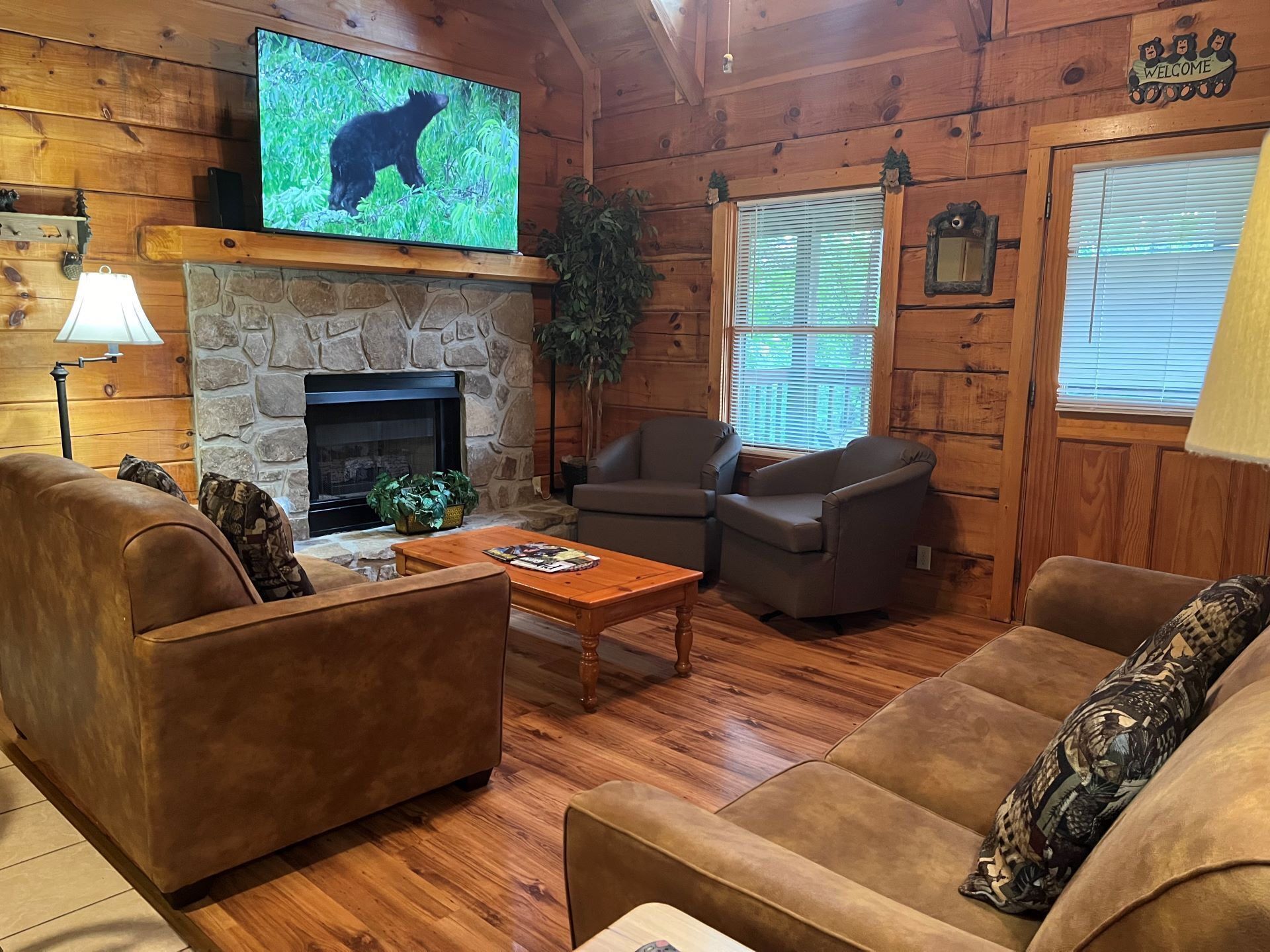 Interior acogedor de una cabaña con chimenea de piedra, paredes de madera y un televisor mostrando un oso.
