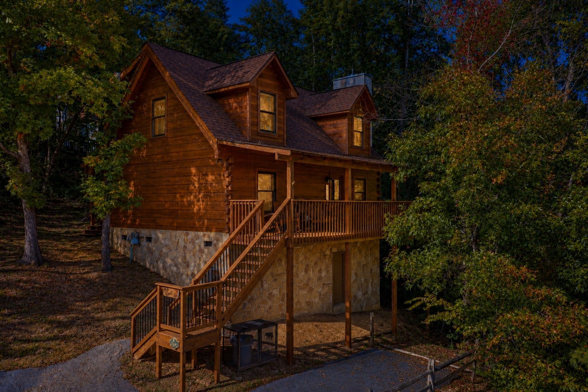 A two-story log cabin with a stone foundation, a wooden deck, and a staircase leading to the upper level.
