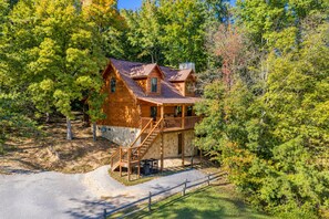 A wooden cabin with a stone foundation, a covered porch, and a staircase leading to the entrance.