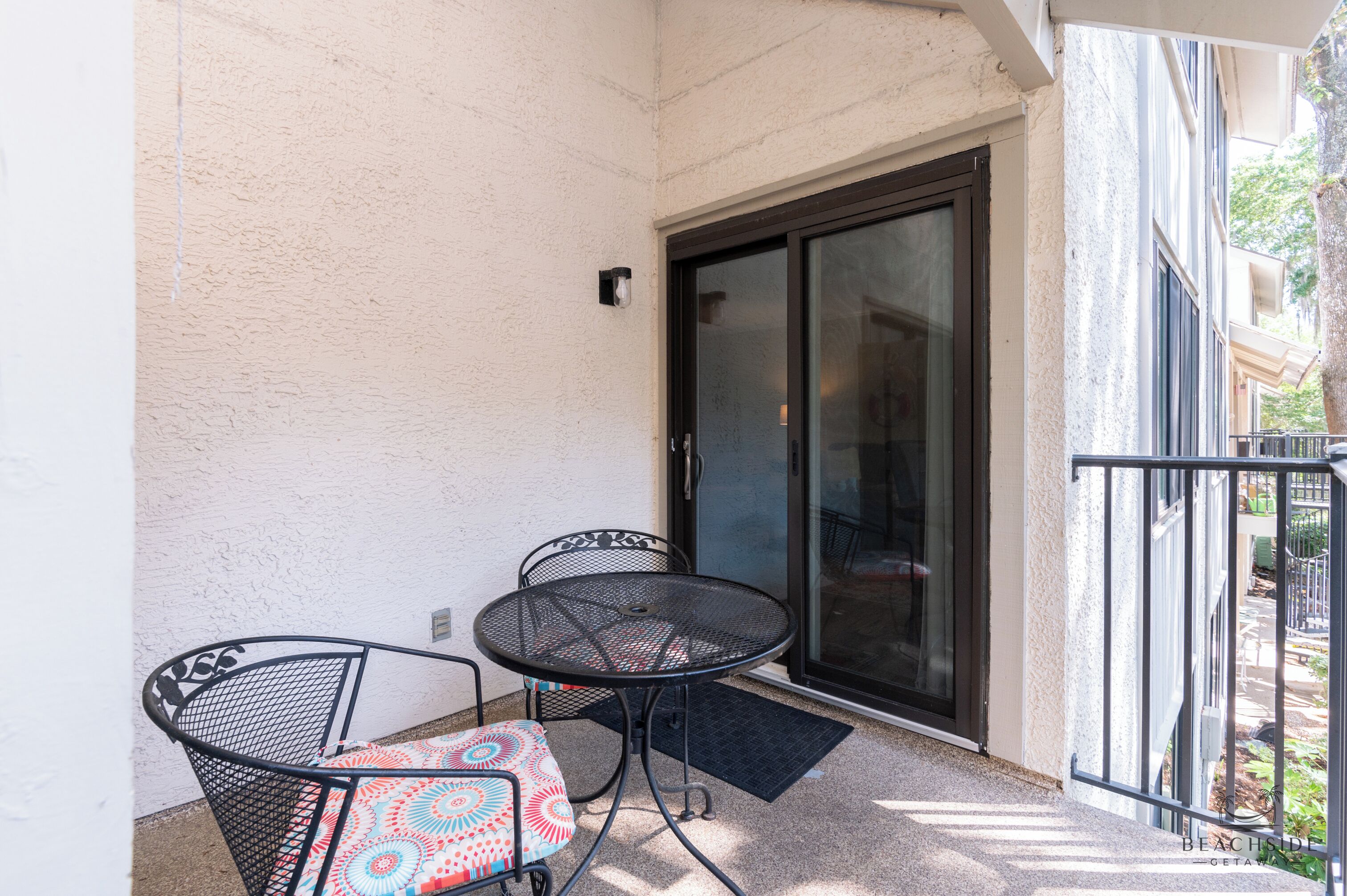 A balcony with a sliding glass door, two metal chairs, and a small table.