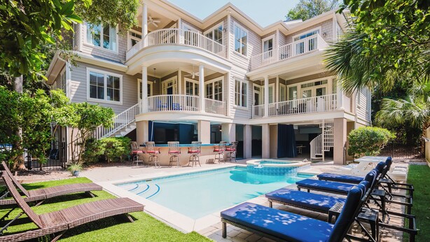 A multi-story building with a swimming pool, outdoor seating, and a well-maintained lawn.