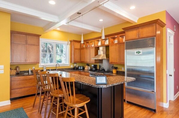 Una cocina con armarios de madera, un refrigerador de acero inoxidable y una isla grande con taburetes de bar.