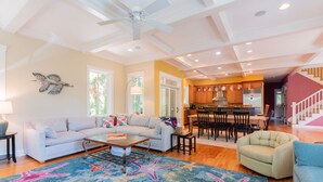 A spacious living room with a large sofa, a coffee table, and a colorful starfish rug. There is a dining area with a table and chairs, and a kitchen in the background.