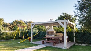 A covered outdoor seating area with a barbecue grill, picnic table, and swing set. - Helios - A paradise in nature. Luxury 2 Bedrooms (Sleeps 4-5) With Pool In Corfu (Agios Mattheos)