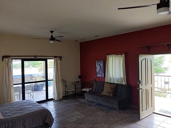 A room with a bed, a sofa, a ceiling fan, a window with curtains, and a door leading outside.