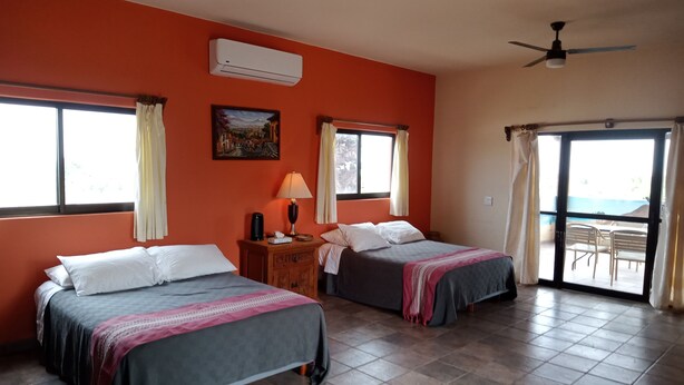 A room with two beds, an air conditioner, a lamp, and a painting on the wall. - Hacienda de Palmas: Room #1 Grande with two queen size beds and sofa bed (La Ribera)