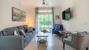 Een woonkamer met een grijze bank, een blauwe fauteuil, een salontafel en een aan de muur bevestigde televisie.